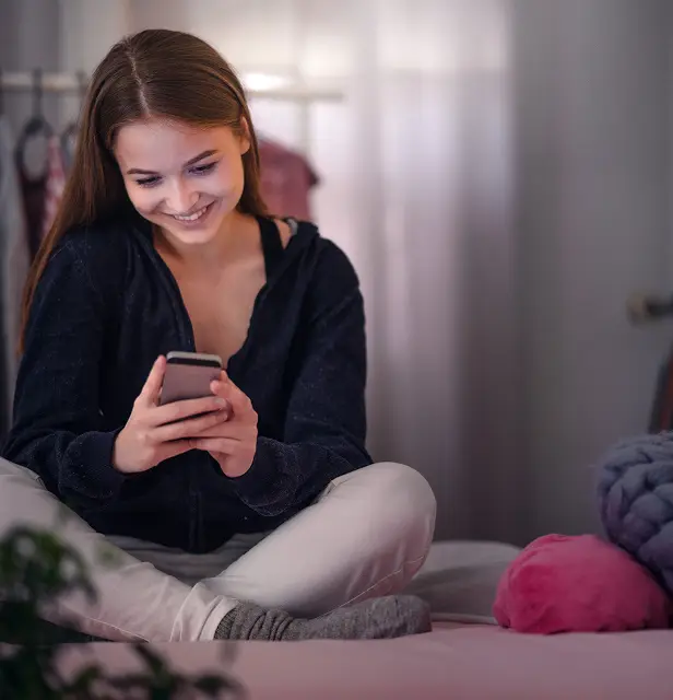 happy young girl using smartphone on bed online