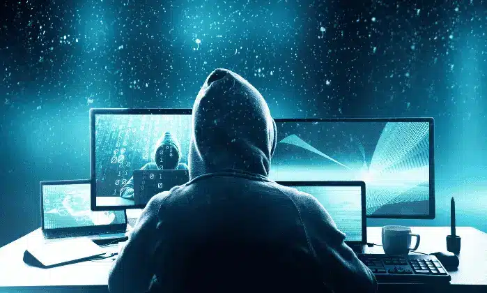 Hoodie sitting in front of multiple computer screens