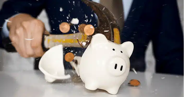 Businessman using a hammer to smash plenty of coins inside piggybank into pieces