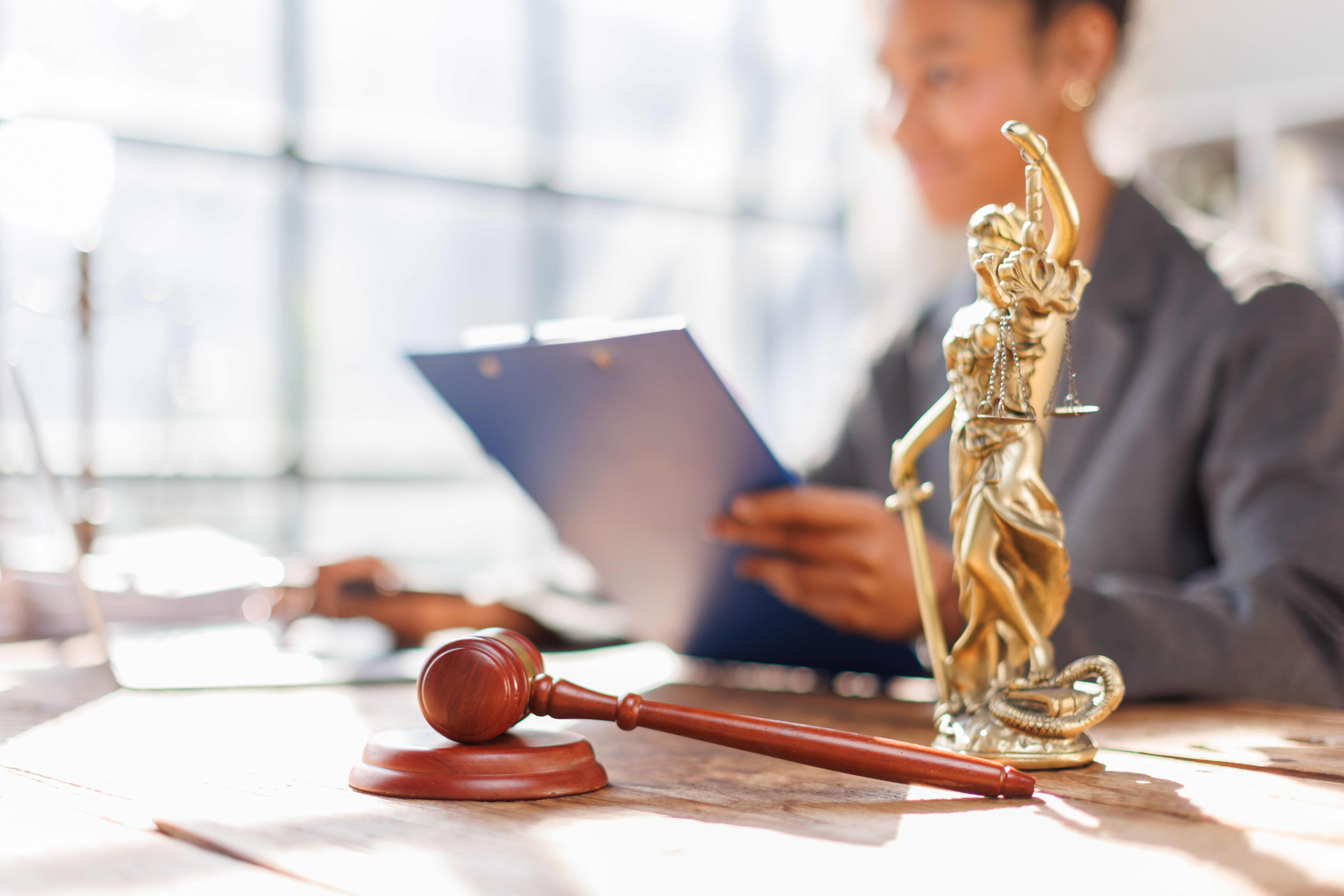 Attractive and confident African American female lawyer holding pen working in office with contract and legal book while sitting at table. Law, legal services, advice, justice and real estate concept.