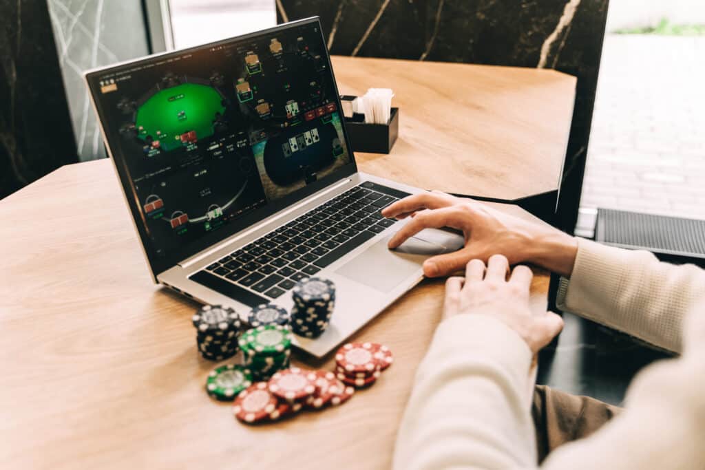 Young man play online poker in laptop. Unrecognizable person.