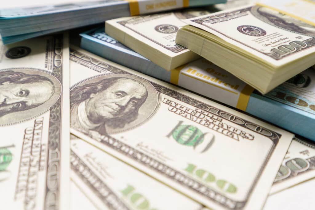 close-up photo of unclaimed class action lawsuit settlement money, hundreds of US dollar bills on a table