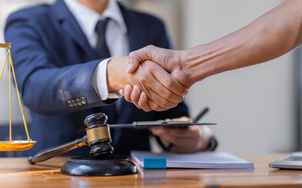 A mass arbitration lawyer shakes hands with a client across a desk. The desk has a gavel on it.