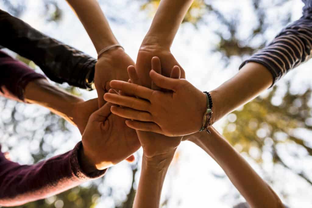 Shot from below of four people stacking hands outside in nature. Concept of unity, togetherness and friendship.
