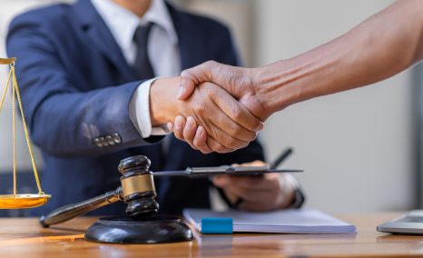 A mass arbitration lawyer shakes hands with a client across a desk. The desk has a gavel on it.