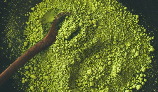 Japanese Matcha green tea powder in dark wooden bowl with spoon, top view, square crop. Clean eating, healthy, diet food concept