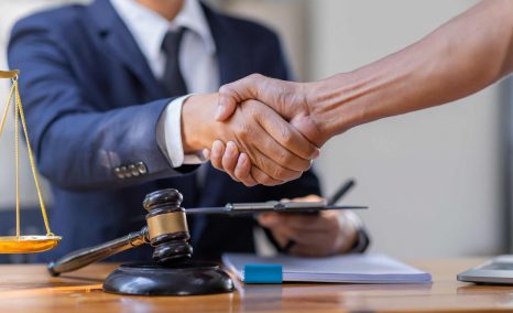 A mass arbitration lawyer shakes hands with a client across a desk. The desk has a gavel on it.