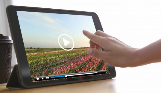 Woman watching video on tablet at wooden desk, closeup